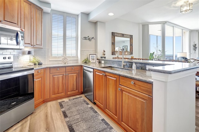 kitchen featuring sink, kitchen peninsula, stone countertops, light hardwood / wood-style flooring, and appliances with stainless steel finishes