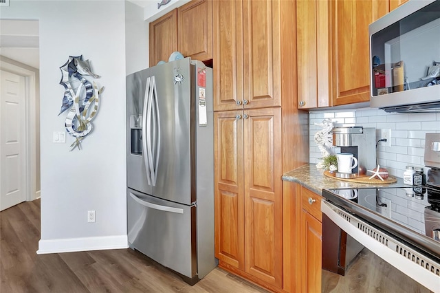 kitchen with light stone countertops, stainless steel appliances, backsplash, and light hardwood / wood-style floors