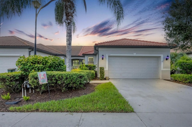 view of front of house with a garage, a tile roof, driveway, and stucco siding