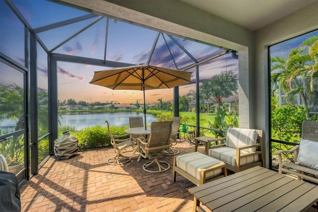 deck at dusk featuring a lanai, a water view, and a patio area