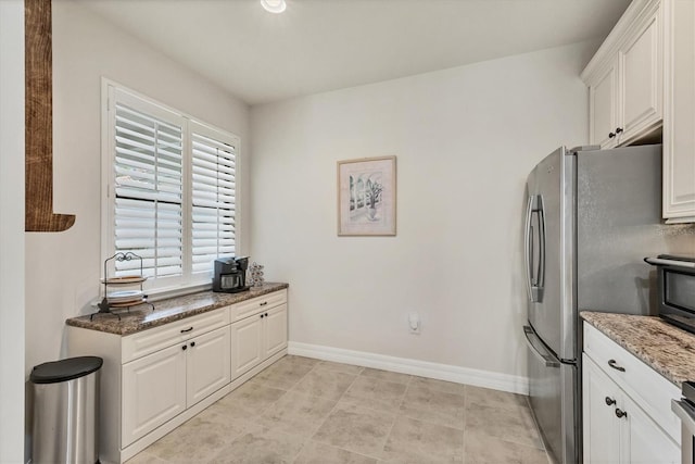 kitchen with white cabinets, dark stone counters, and stainless steel fridge