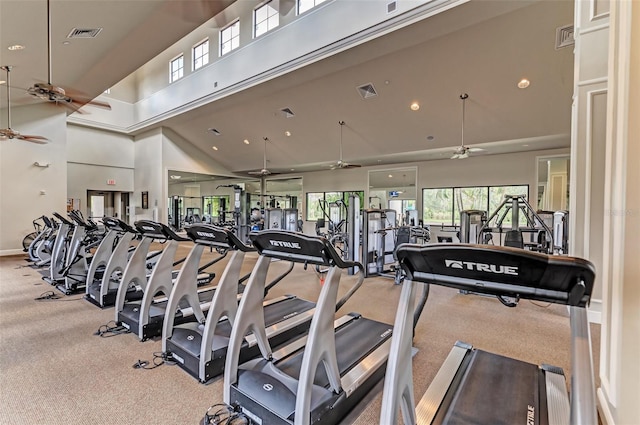 workout area featuring a towering ceiling, ceiling fan, and light colored carpet