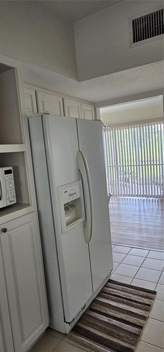 kitchen with light tile patterned floors, white appliances, white cabinetry, and tile counters