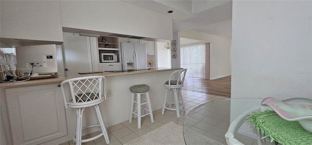 kitchen featuring white cabinets, a kitchen bar, white appliances, and light tile patterned flooring