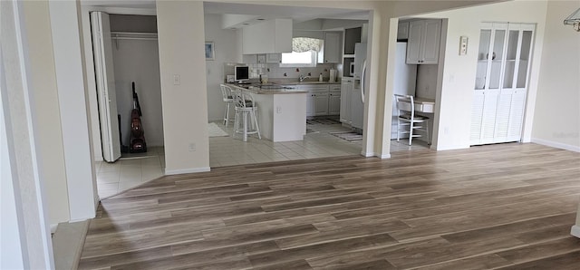 interior space with backsplash, gray cabinetry, a breakfast bar, dark wood-type flooring, and white refrigerator with ice dispenser