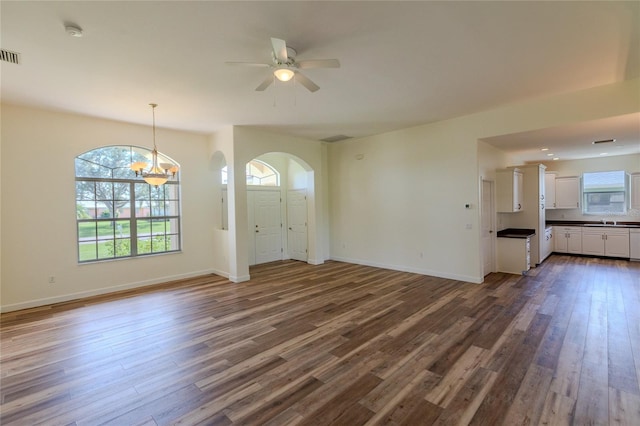 unfurnished living room featuring ceiling fan with notable chandelier, plenty of natural light, and dark wood-type flooring