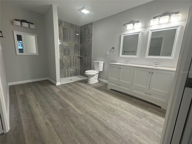 bathroom with hardwood / wood-style flooring, tiled shower, vanity, and toilet