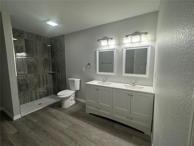 bathroom featuring a tile shower, wood-type flooring, toilet, and vanity