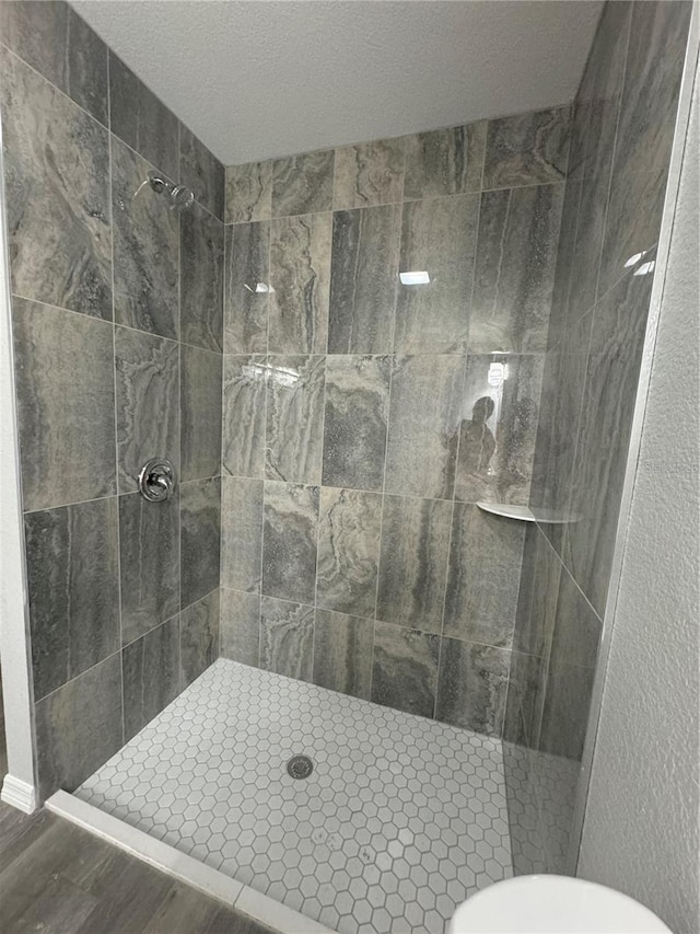 bathroom with toilet, tiled shower, and wood-type flooring