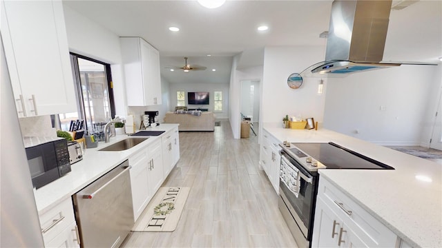 kitchen with appliances with stainless steel finishes, white cabinetry, island range hood, ceiling fan, and sink