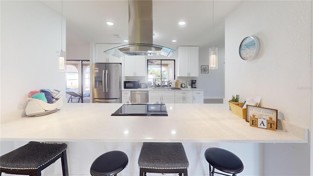 kitchen featuring white cabinets, kitchen peninsula, island exhaust hood, appliances with stainless steel finishes, and a breakfast bar area