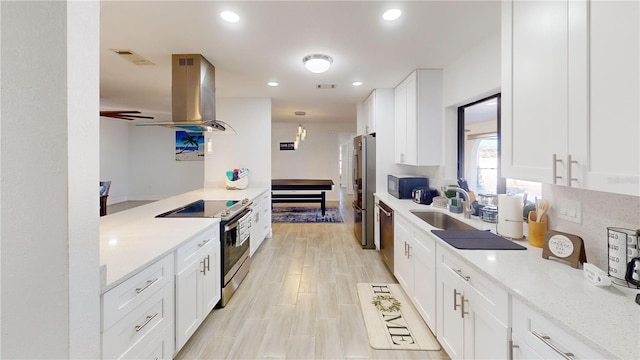 kitchen featuring appliances with stainless steel finishes, island range hood, white cabinetry, and light stone countertops