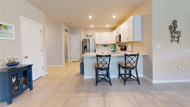 kitchen with a breakfast bar, stainless steel appliances, light countertops, white cabinets, and a peninsula