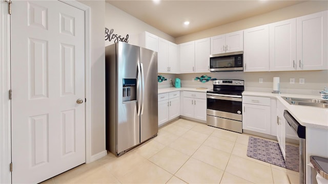 kitchen with white cabinets, appliances with stainless steel finishes, light countertops, a sink, and light tile patterned flooring