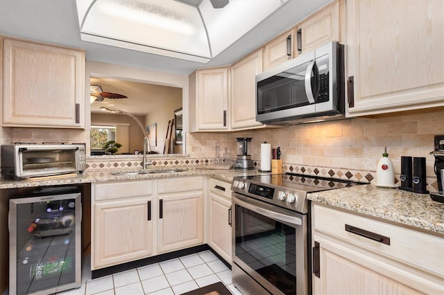 kitchen featuring sink, wine cooler, light brown cabinetry, light tile patterned floors, and appliances with stainless steel finishes