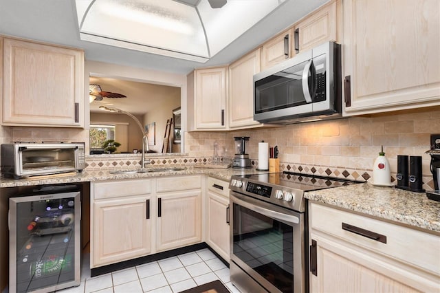 kitchen with beverage cooler, a sink, appliances with stainless steel finishes, light brown cabinetry, and tasteful backsplash