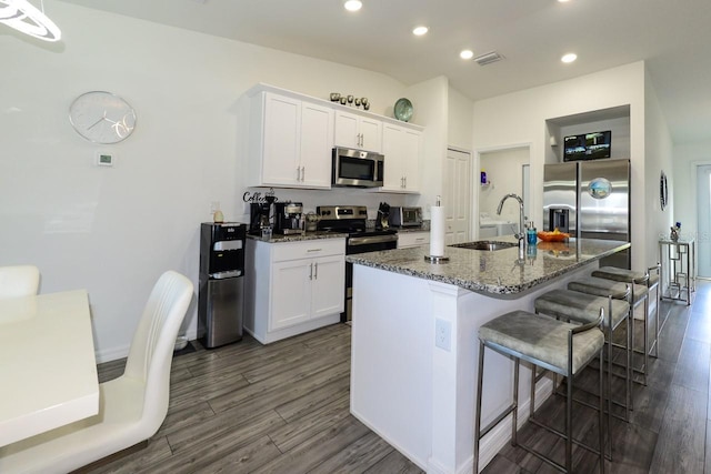 kitchen with an island with sink, appliances with stainless steel finishes, dark hardwood / wood-style floors, and a breakfast bar