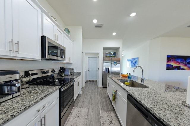 kitchen with light stone counters, white cabinets, sink, stainless steel appliances, and light hardwood / wood-style floors