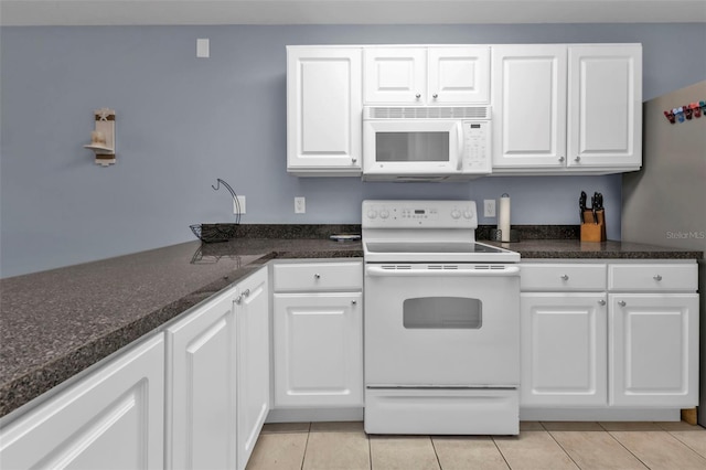 kitchen with dark stone countertops, white appliances, white cabinetry, and light tile patterned flooring