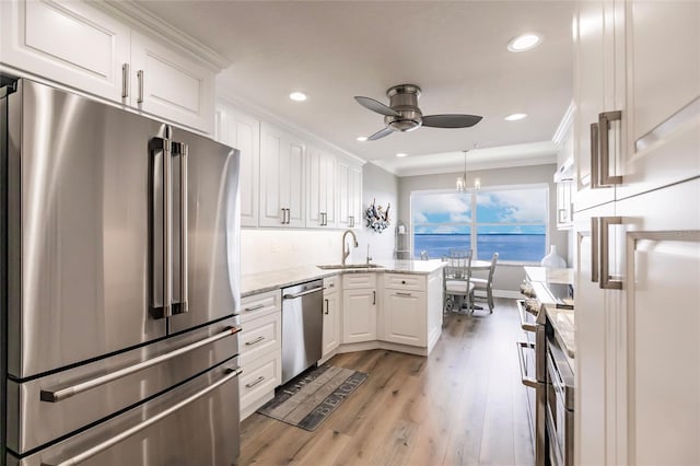 kitchen with white cabinetry, ceiling fan with notable chandelier, a sink, high quality appliances, and a peninsula