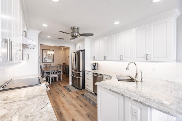 kitchen featuring light wood-type flooring, stainless steel appliances, ceiling fan with notable chandelier, a sink, and white cabinets