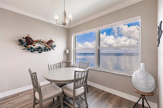 dining area with crown molding, a water view, baseboards, a chandelier, and wood finished floors
