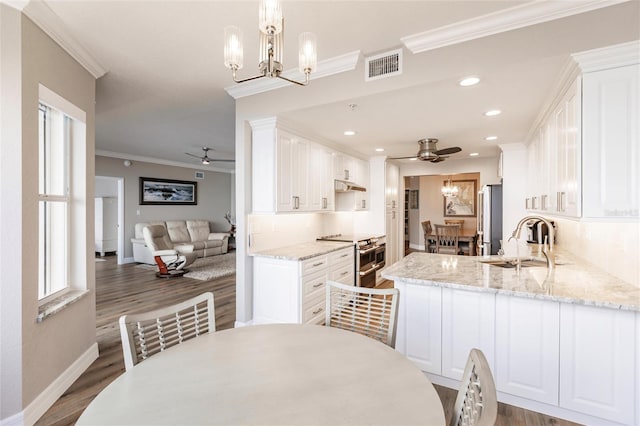 dining area featuring dark hardwood / wood-style floors, ceiling fan with notable chandelier, ornamental molding, and sink