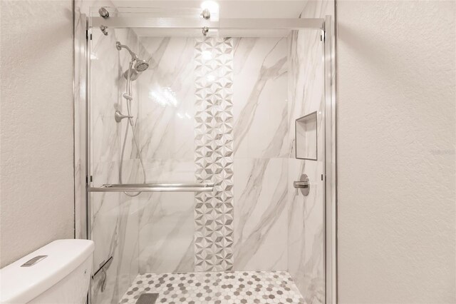 full bath with a textured wall, a marble finish shower, and toilet