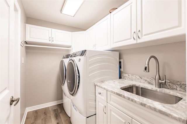 laundry area featuring a sink, baseboards, washer and dryer, light wood-style floors, and cabinet space