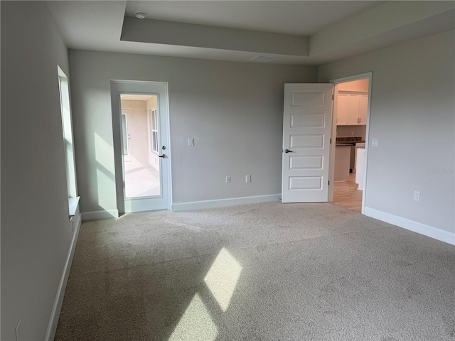 carpeted empty room featuring a raised ceiling and baseboards