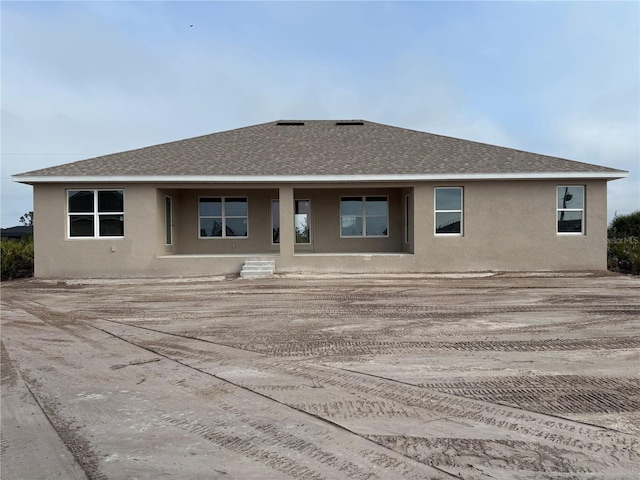 back of house featuring a shingled roof and stucco siding