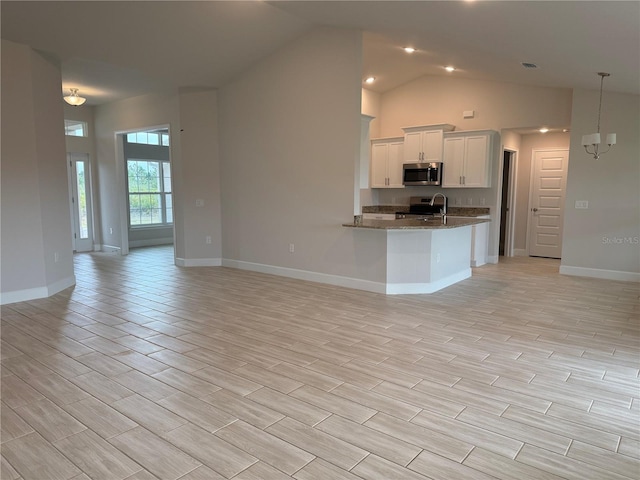 kitchen with open floor plan, dark stone countertops, wood tiled floor, stainless steel appliances, and white cabinetry