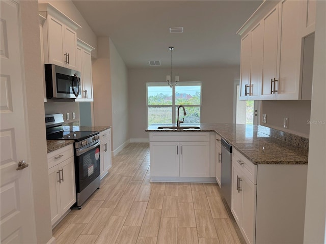 kitchen featuring a peninsula, a sink, white cabinets, appliances with stainless steel finishes, and dark stone counters