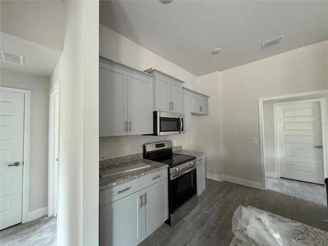 kitchen featuring light stone counters, dark hardwood / wood-style flooring, stainless steel appliances, and gray cabinetry