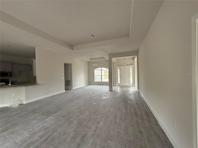 unfurnished living room with an inviting chandelier, hardwood / wood-style floors, and a raised ceiling