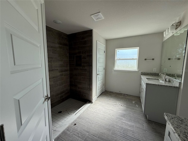 bathroom featuring vanity, hardwood / wood-style flooring, a textured ceiling, and tiled shower