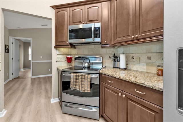 kitchen featuring stainless steel appliances, light stone counters, backsplash, vaulted ceiling, and light wood-type flooring