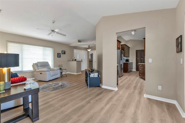 living room with ceiling fan, vaulted ceiling, and light wood-type flooring