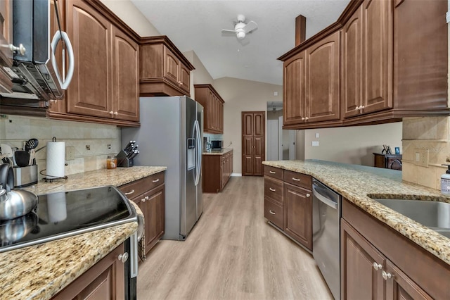 kitchen featuring lofted ceiling, backsplash, light stone countertops, appliances with stainless steel finishes, and light hardwood / wood-style floors