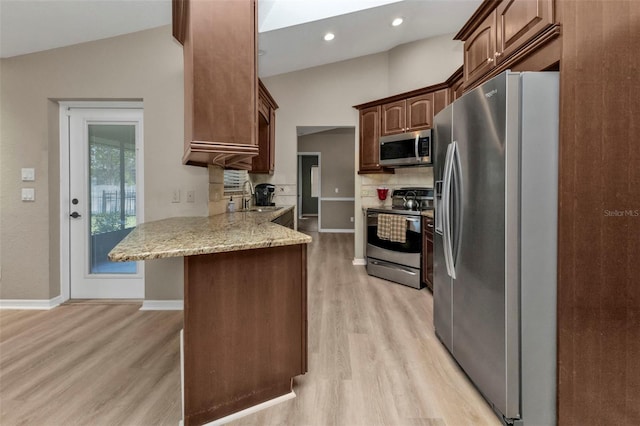 kitchen with lofted ceiling with skylight, sink, light hardwood / wood-style flooring, light stone counters, and stainless steel appliances