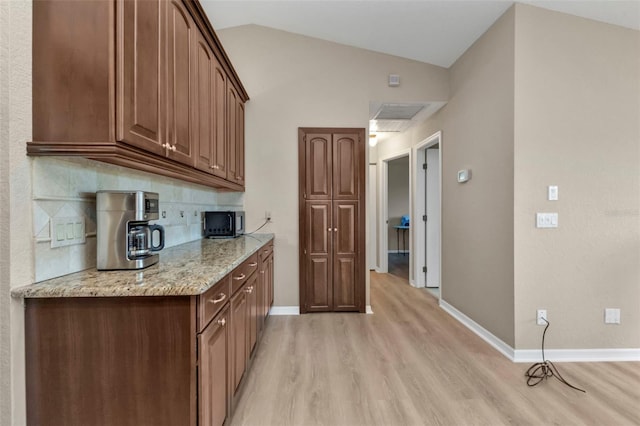 kitchen with light hardwood / wood-style floors, vaulted ceiling, tasteful backsplash, and light stone counters