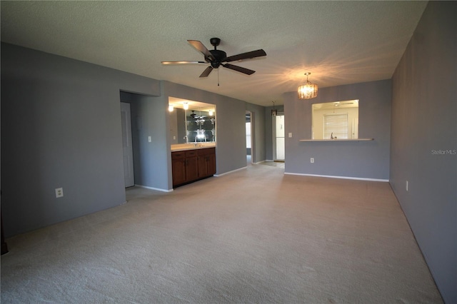 unfurnished living room featuring a textured ceiling, ceiling fan with notable chandelier, and light colored carpet