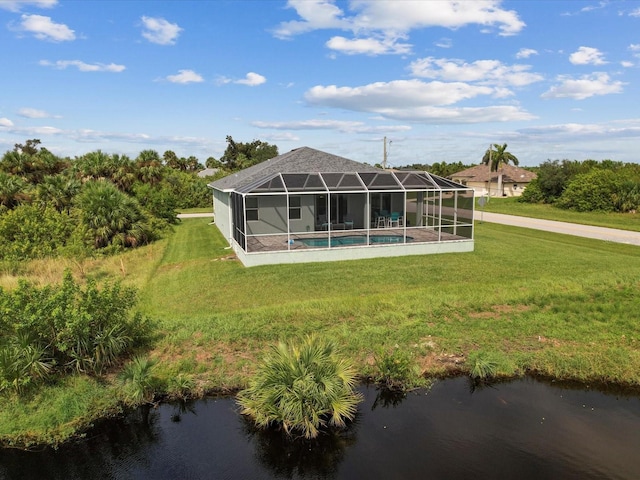 rear view of house with glass enclosure, a water view, and a yard