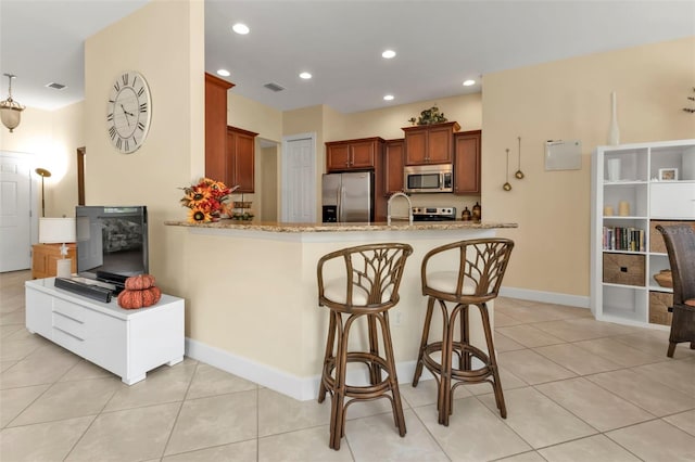 kitchen featuring a breakfast bar area, kitchen peninsula, stainless steel appliances, light tile patterned floors, and light stone countertops