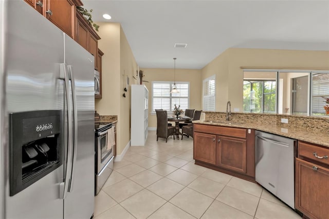 kitchen with light tile patterned floors, appliances with stainless steel finishes, light stone counters, decorative light fixtures, and a sink