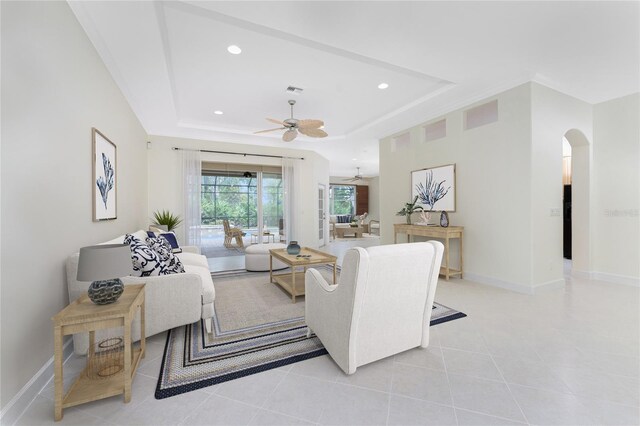 living area featuring recessed lighting, a tray ceiling, arched walkways, baseboards, and ceiling fan