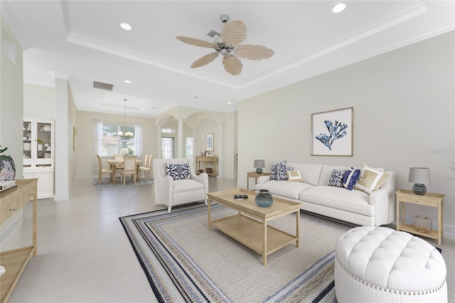 living room with tile patterned flooring, ceiling fan with notable chandelier, a raised ceiling, and crown molding