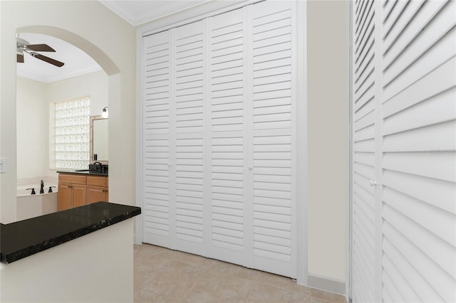 interior space featuring arched walkways, dark countertops, ceiling fan, crown molding, and light tile patterned floors