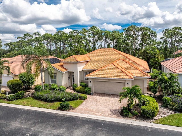 mediterranean / spanish house featuring an attached garage, a tile roof, stucco siding, and driveway