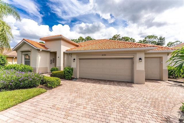 mediterranean / spanish home featuring a garage, a tiled roof, and decorative driveway